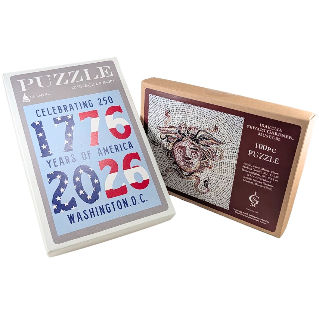 Two museum puzzle boxes—white ‘1776–2026’ and kraft Medusa mosaic—photographed side by side.